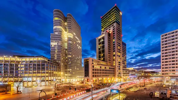 Abendliche Stimmung zur blauen Stunde: Weitwinklige Aufnahme der Berliner Hochhäuser Upper West und Zoofenster. Moderne Hochhäuser unterschiedlichen Stils in einem urbanen Umfeld mit Straße im Vorderung und weiteren flacheren Gebäuden.