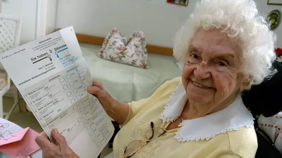 Symbolbild: Seniorin hält Stimmzettel in der Hand und lächelt