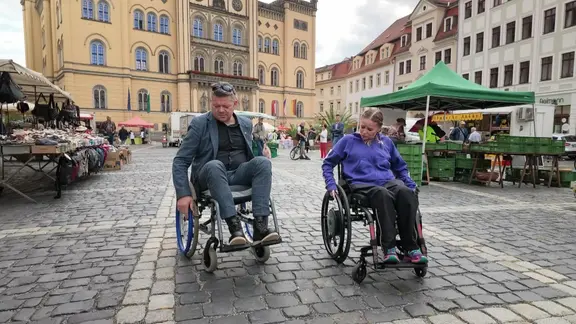 Ein Mann und eine Frau fahren mit dem Rollstuhl durch Zittau. 