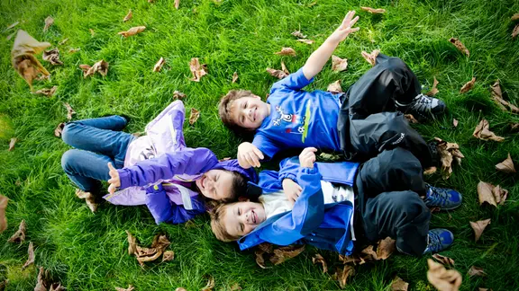 Drei Kinder liegen auf einer Wiese mit Laub