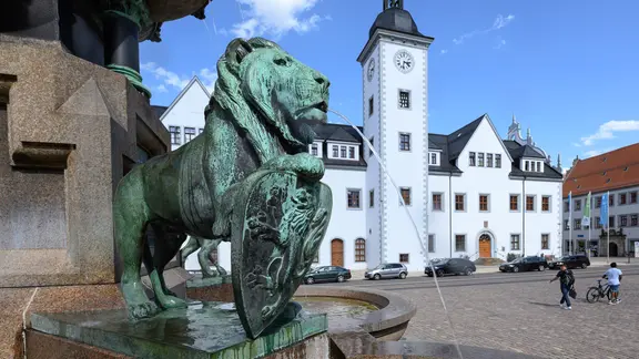 Ein wasserspeiender Löwe, dahinter das Rathaus Freiberg.
