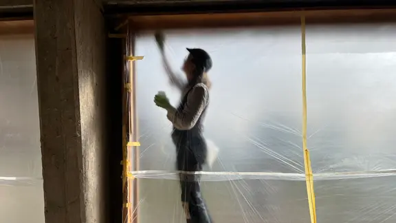 Eine Frau steht hinter einer Folie an einer Fensterrahmen.