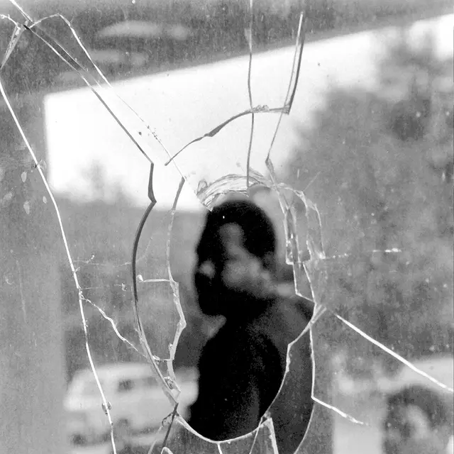 Hoyerswerda 1991: Eine eingeworfene Glasscheibe, dahinter sitzt ein Schwarzer Mann