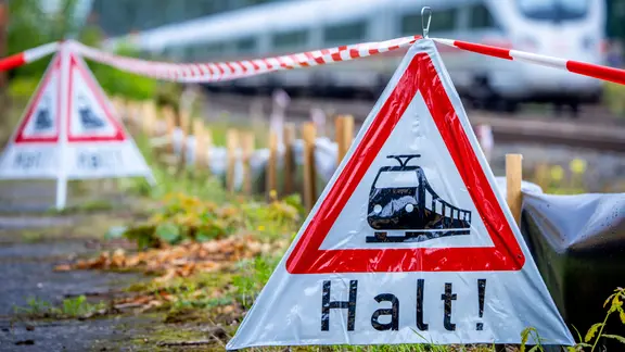Rote Warndreiecke mit einem Zug und der Schrift "Halt!", im Hintergrund unscharf ein Zug