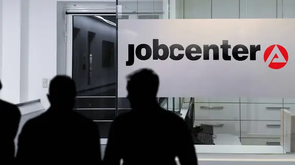 Menschen, die vor einem Jobcenter stehen.
