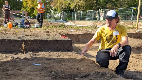 Thomas Lukas zeigt auf ein menschliches Skellett in einer Ausgrabungstätte.