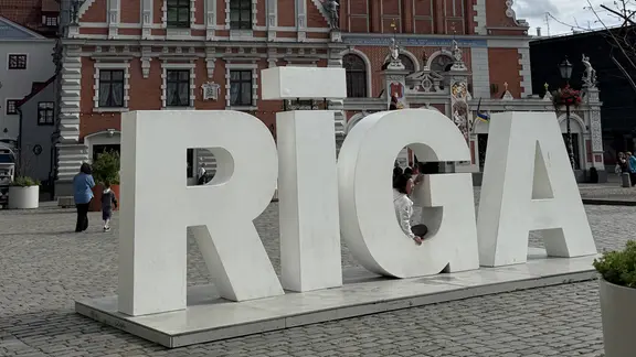 Die Buchstaben "Riga" vor einem historischen roten Haus.