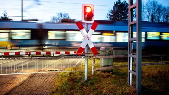 Ein Nahverkehrszug passiert einen geschlossenen Bahnübergang.