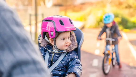 Ein lächelndes Mädchen mit Helm sitzt auf dem Kindersitz eines Fahrrads