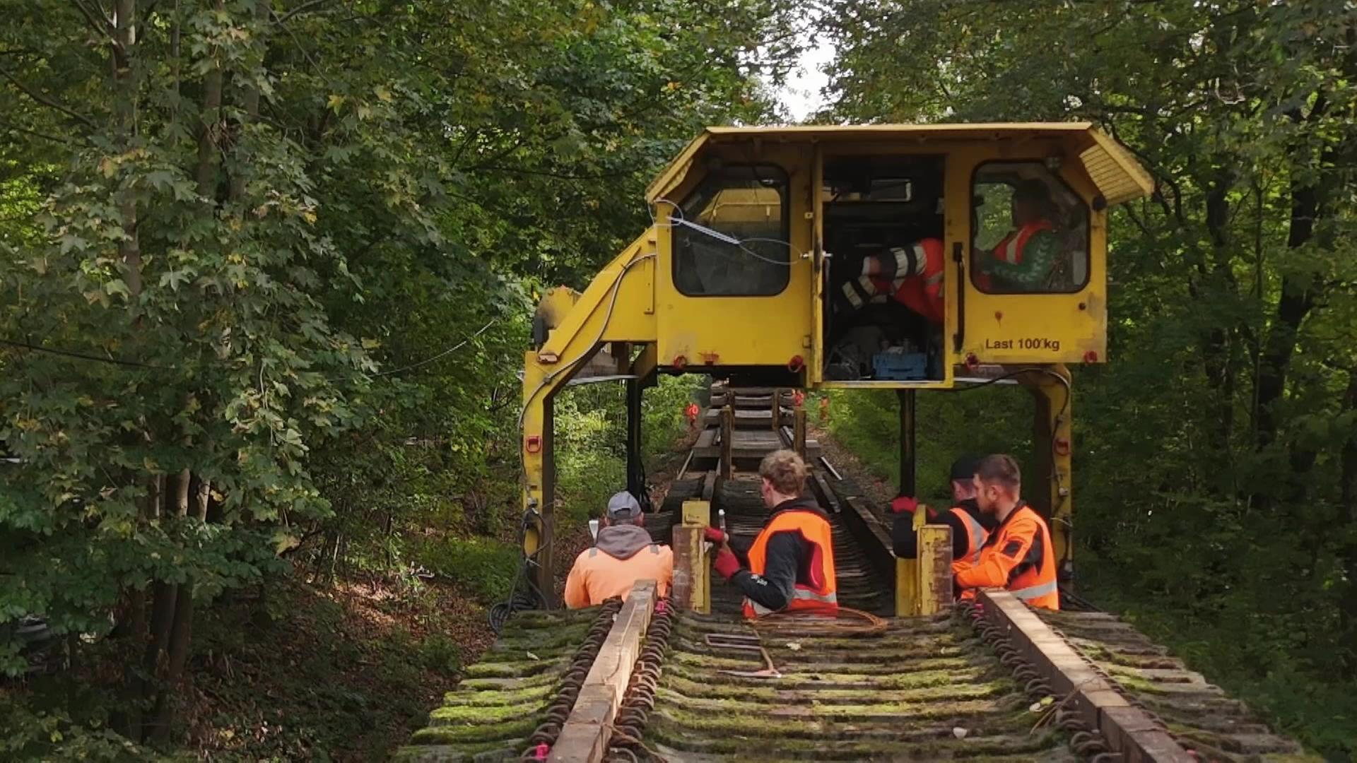 Männer stehen vor einen Eisenbahn-Bauzug, davor ist ein Gleis mit Schwellen zu sehen.  | MDR SACHSENSPIEGEL