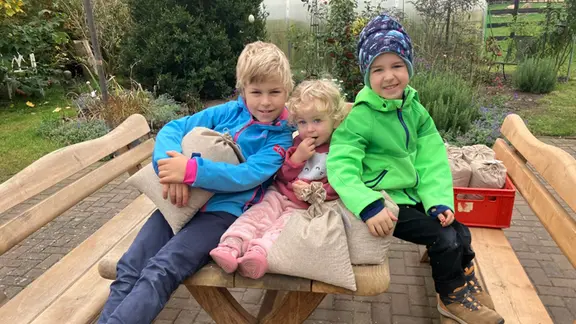 Drei Kinder sitzen auf auf einem Tisch in einem Garten.