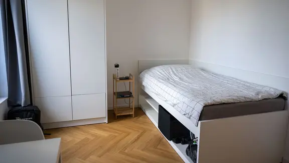 In einer modern eingerichteten Werkswohnung steht ein Bett, ein Nachttisch, ein Schreibtisch und ein Kleiderschrank