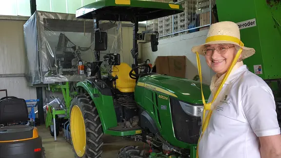 Eine Frau mit Sonnenhut steht in einer großen Garage vor einem grünen Traktor