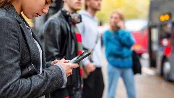 Menschen stehen wartend an einer Bushaltestelle und nutzen ihre Smartphones