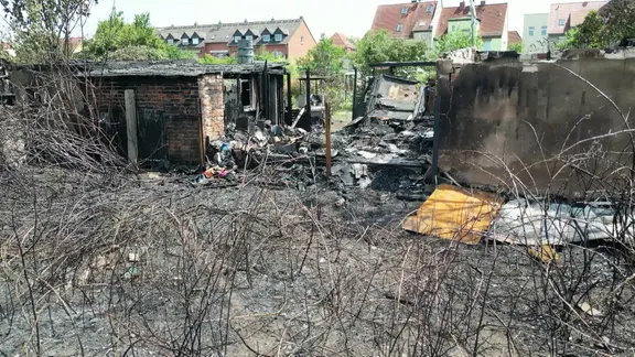 Mehrere Gartenlauben sind verkohlt, es liegt Schutt herum.