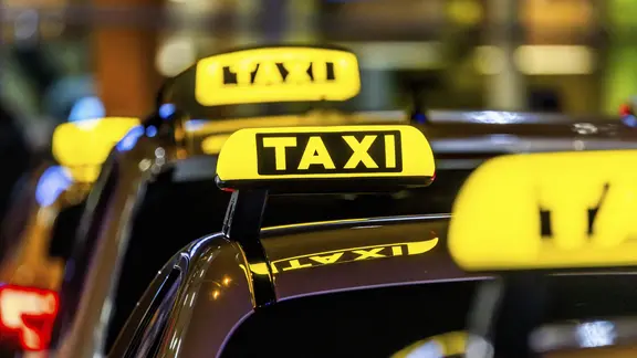 Taxis mit leuchtenden Taxischildern warten nachts an einem Taxistand auf Fahrgäste.