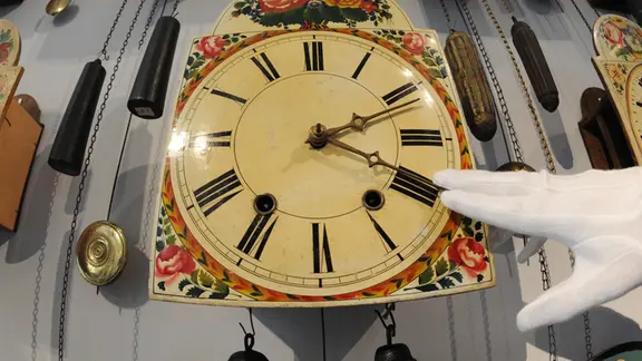 Ein Uhrmacher verstellt an einer Uhr die Zeiger.