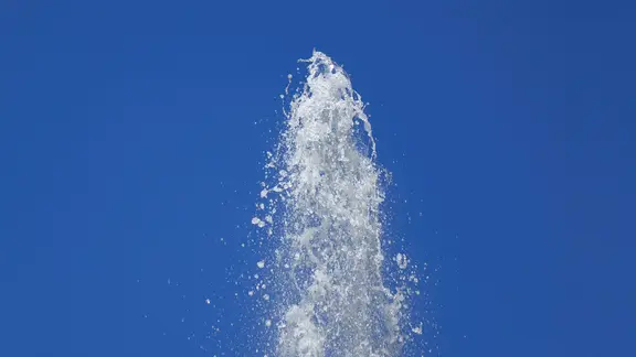 Vor einem blauen Himmel befindet sich die Spitze einer Fontaene.