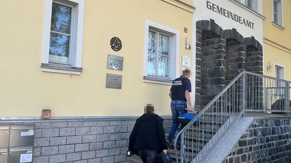 Polizisten laufen die Treppe des Gemeindeamts in Langenwolschendorf hoch.