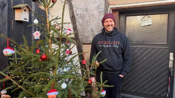 Sebastian Albert steht lachend neben einem Weihnachtsbaum.