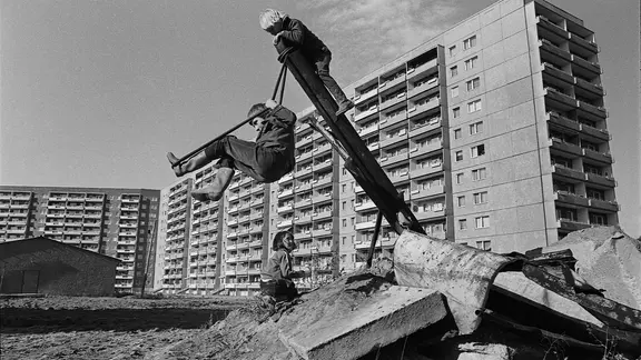 Kinder spielen auf Schuttplatz vor Plattenbau.
