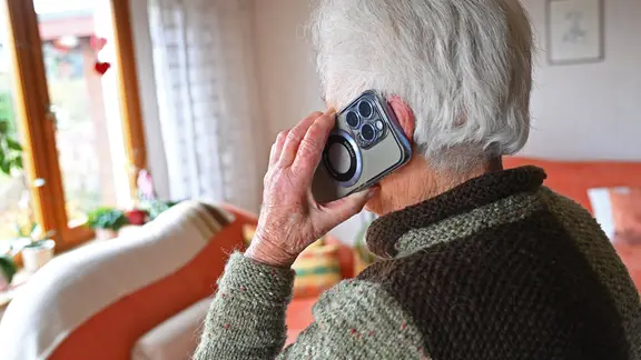 Alte Frau hält ein Smartphone ans Ohr. 