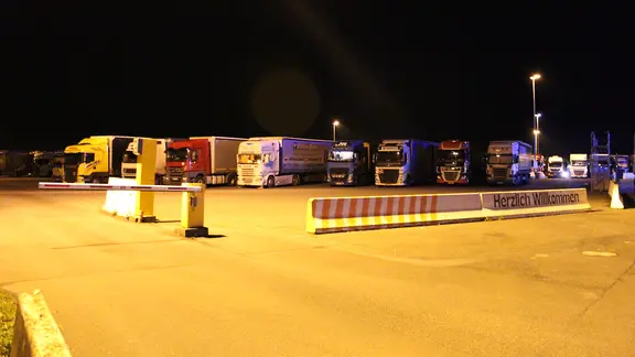 Ein Autobahn-Parkplatz voller Lkw bei Nacht

