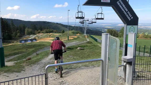 Unter einem Sessellift fährt ein Mountainbiker auf einer Schotterpiste in der "Bikewelt Schöneck".