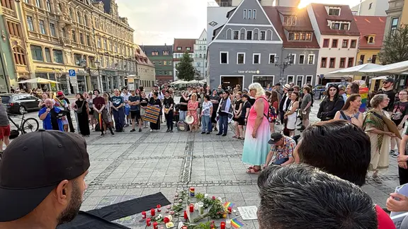 Menschen stehen bei einem Gedenken in einer Innenstadt. 