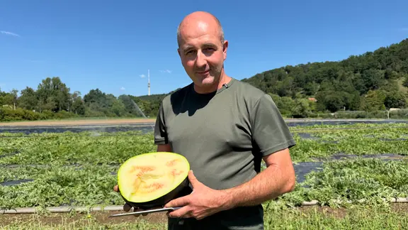 Ein Mann steht auf einem Feld und hält eine Wassermelone in der Hand. 