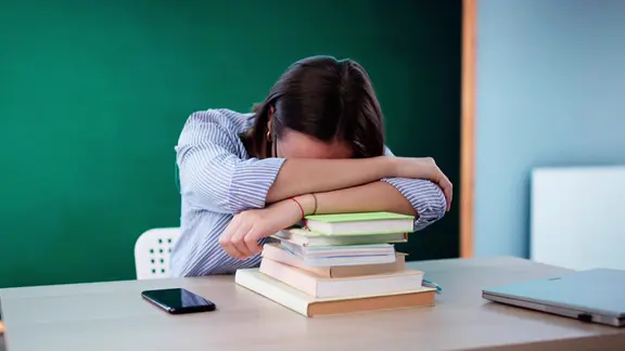 Eine Person liegt mit den Kopf auf einen Stappel Bücher.