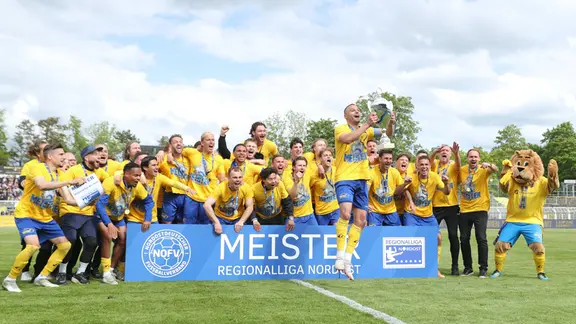 Djamal Ziane (13, Lok Leipzig) stemmt den Meister-Pokal in die Luft, während das Lok-Team dahinter jubelt und feiert. 