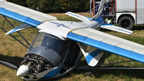 Ein abgestürztes Ultraleichtflugzeug auf einer Wiese vor einem Feuerwehrfahrzeug