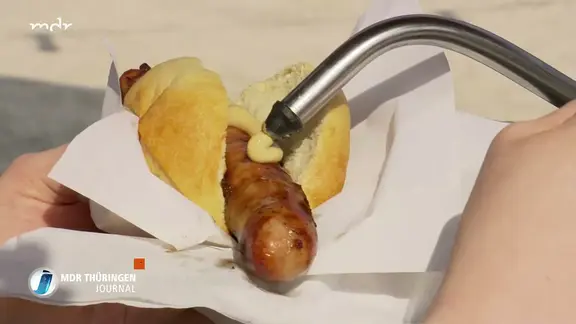 Mit Senfspender wird Senf auf eine Bratwurst gespritzt
