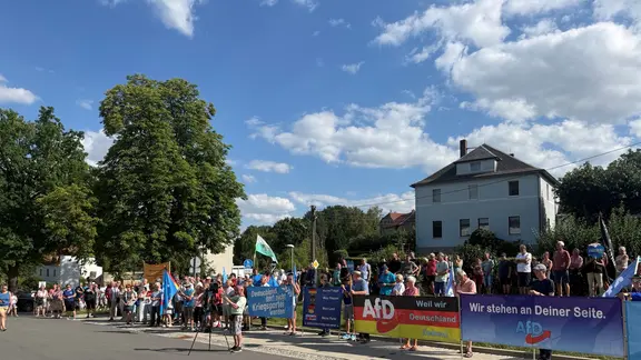 Menschen mit Transparenten, darujter mit AfD-Aufschrift, stehen an einer Straße