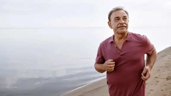 Nachdenklicher älterer Mann läuft am Strand am Meer entlang.