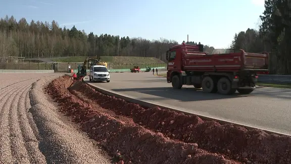 Ein LKW ein Kleintransporter und ein Minibagger stehen auf der Sachsenring-Rennstrecke.