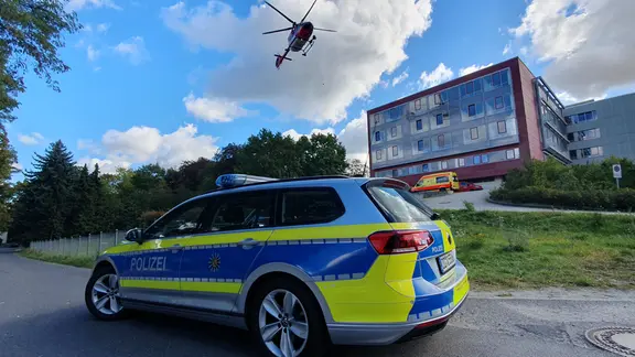 Ein Polizeifahrzeug steht auf einer Sttraße vor dem Landay Gymnasium. Am Himmel fliegt ein Hubschrauber.