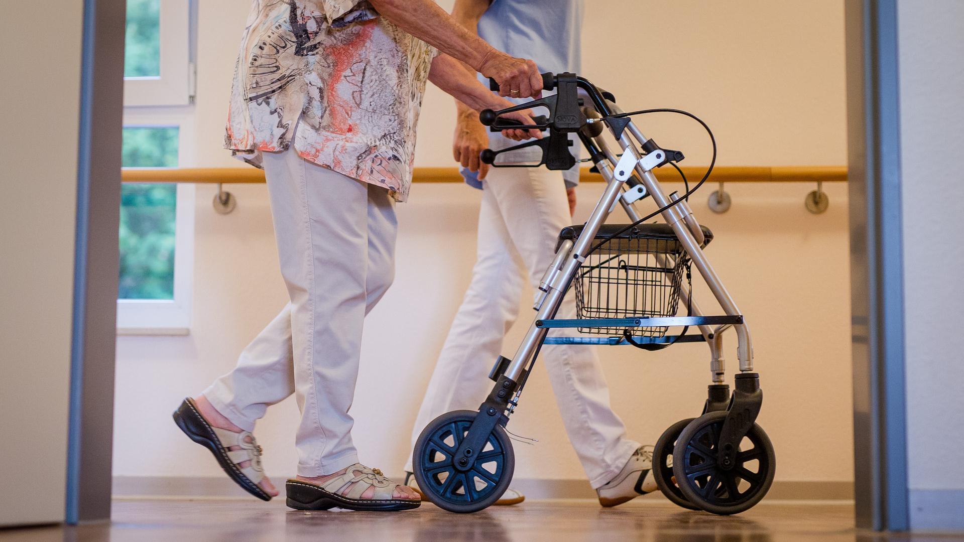 Eine Pflegekraft geht in einem Pflegeheim mit einer älteren Dame über einen Korridor. (zu dpa: 