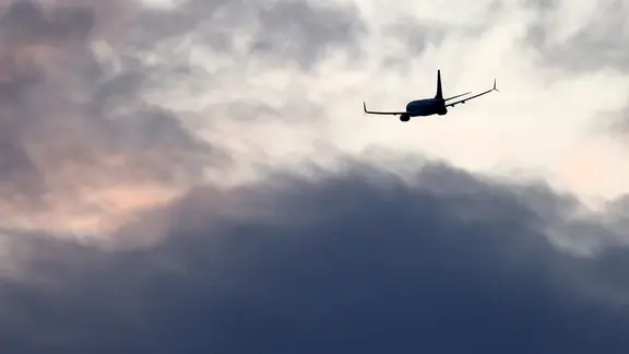 Ein Flugzeug startet vor einem Sonnenuntergang mit grauen Wolken.