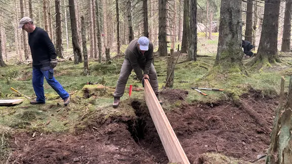 Männer verschließen einen Entwässerungsgraben mit einem Holzbrett