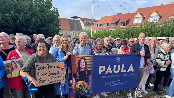 Menschen am Straßenrand mit Platen für die deutsche Weinkönigin Paula