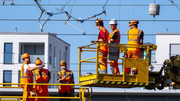 Arbeiter auf einer Hebebühne reparieren eine abgerissene Oberleitung.