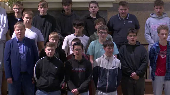 Schüler einer Klasse singen gemeinsam mit einem Musiker auf einem Chorpodest