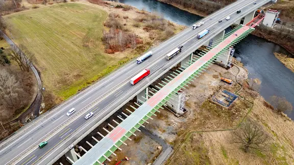 Autos fahren über die alte vierspurige Brücke über die Mulde. Rechts daneben zieht sich der Rohbau für die erste neue Brückenhälfte über den Fluss.