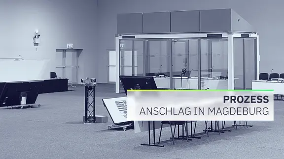 Leere Sitzreihen in einem temporären Gerichtssaal, eine Sicherheitszelle in der Ecke des Saales