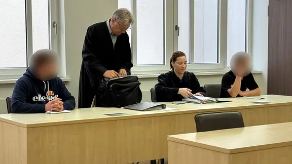 Zwei Angeklagte mit ihren Anwälten sitzen in einem Gerichtssaal