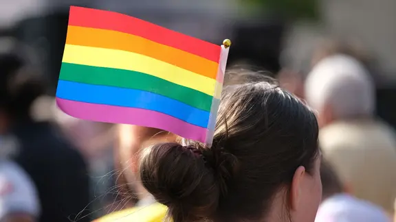 Eine CSD-Teilnehmerin trägt ein Regenbogenfähnchen in ihrem Haarknoten. 