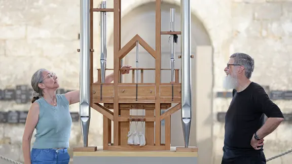 Zwei Personen stehen neben einer Konstruktion aus Holz und Orgelpfeifen.