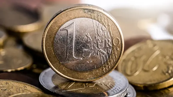 Eine 1 Euro Münze steht auf mehreren anderen Münzen.